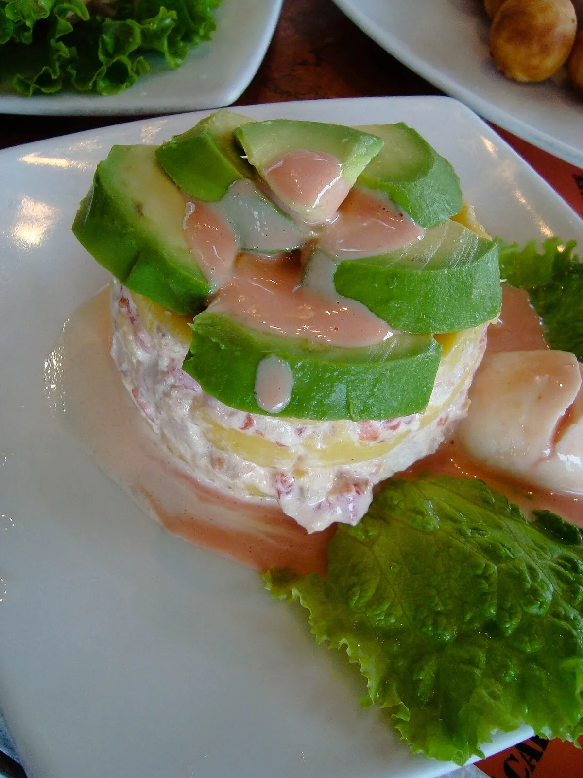 Causa de papa amarilla cubierta con palta y salsa acevichada