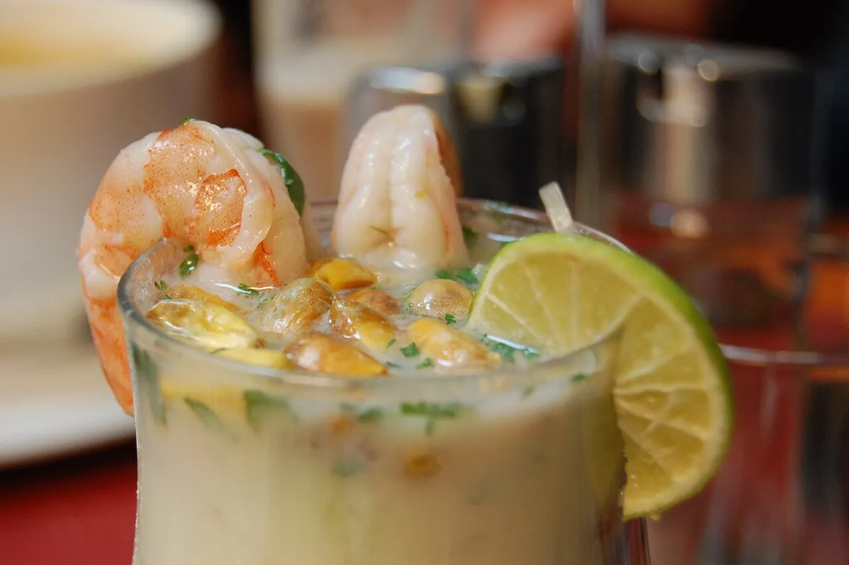 Leche de tigre servida en vaso con langostinos y limón